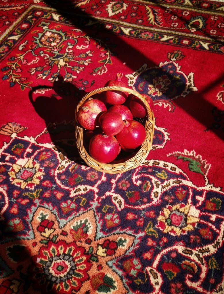A basket of fresh red apples sits on an ornate Persian rug, highlighted by warm sunlight.